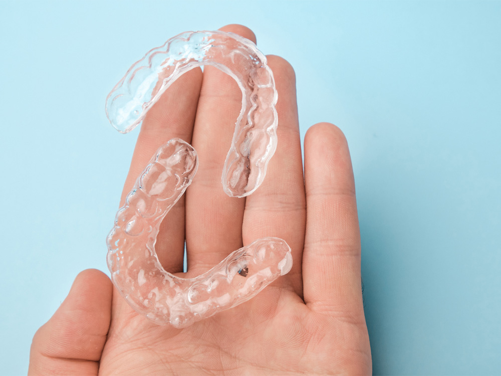 A hand holding a pair of Invisalign retainers with a light blue background